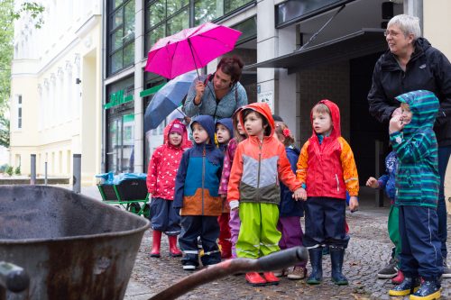 Eine Gruppe Kinder mit Erzieherinnen in Regenjacken und mit Regenschirmen läuft durch die Stadt