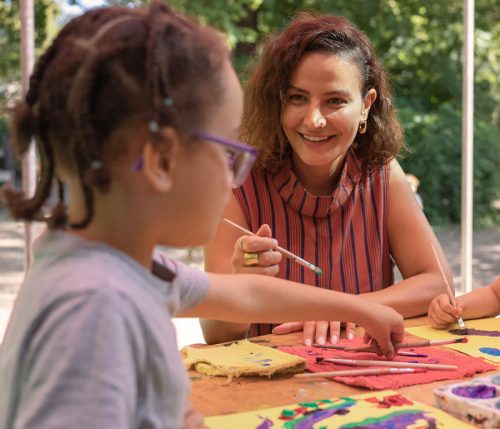 Eine Pädagogin malt zusammen mit Kindern auf Textilien
