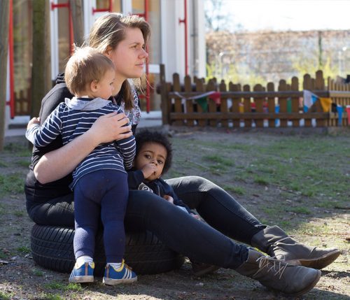 Eine Erzieherin sitzt mit Kindern draußen und hält sie im Arm