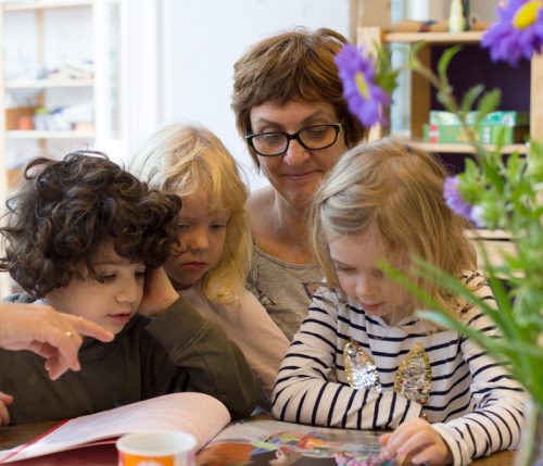 Eine Erzieherin im Kindergarten schaut zusammen mit drei Kindern in ein Buch