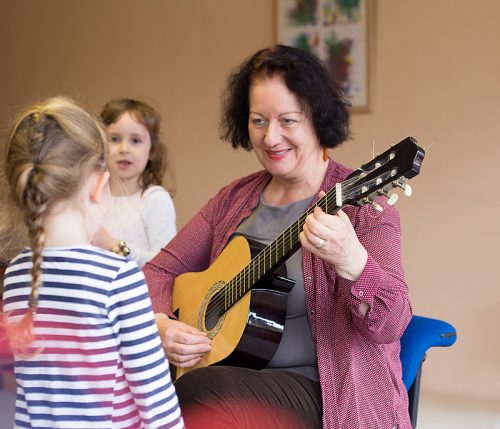 Eine Pädagogin spielt einem Mädchen ein Lied auf der Gitarre