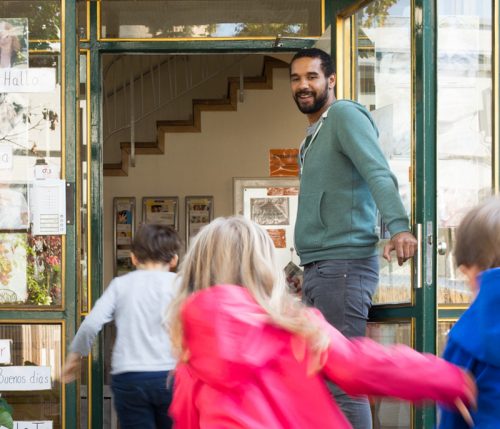 Eine Pädagogische Fachkraft öffnet die Tür für hineinrennende Kinder