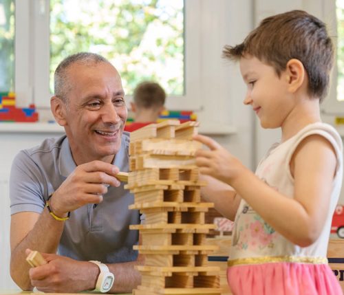 Ein Erzieher spielt mit einem Kind mit Holz-Bauklötzen