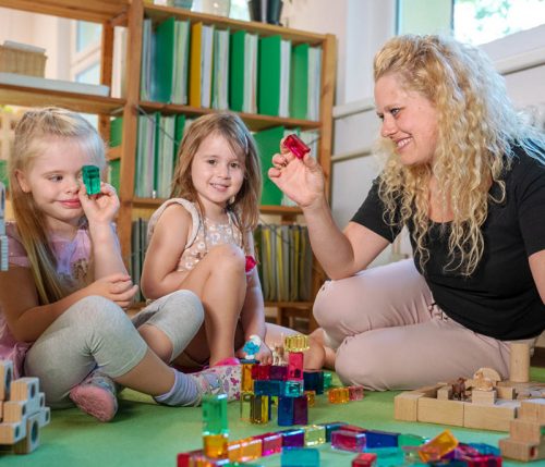 Eine pädagogische Fachkraft spielt mit zwei Mädchen mit Bausteinen